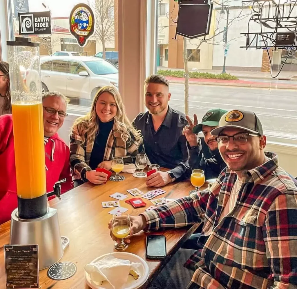 A group of friends with drinks and a card game at a window table